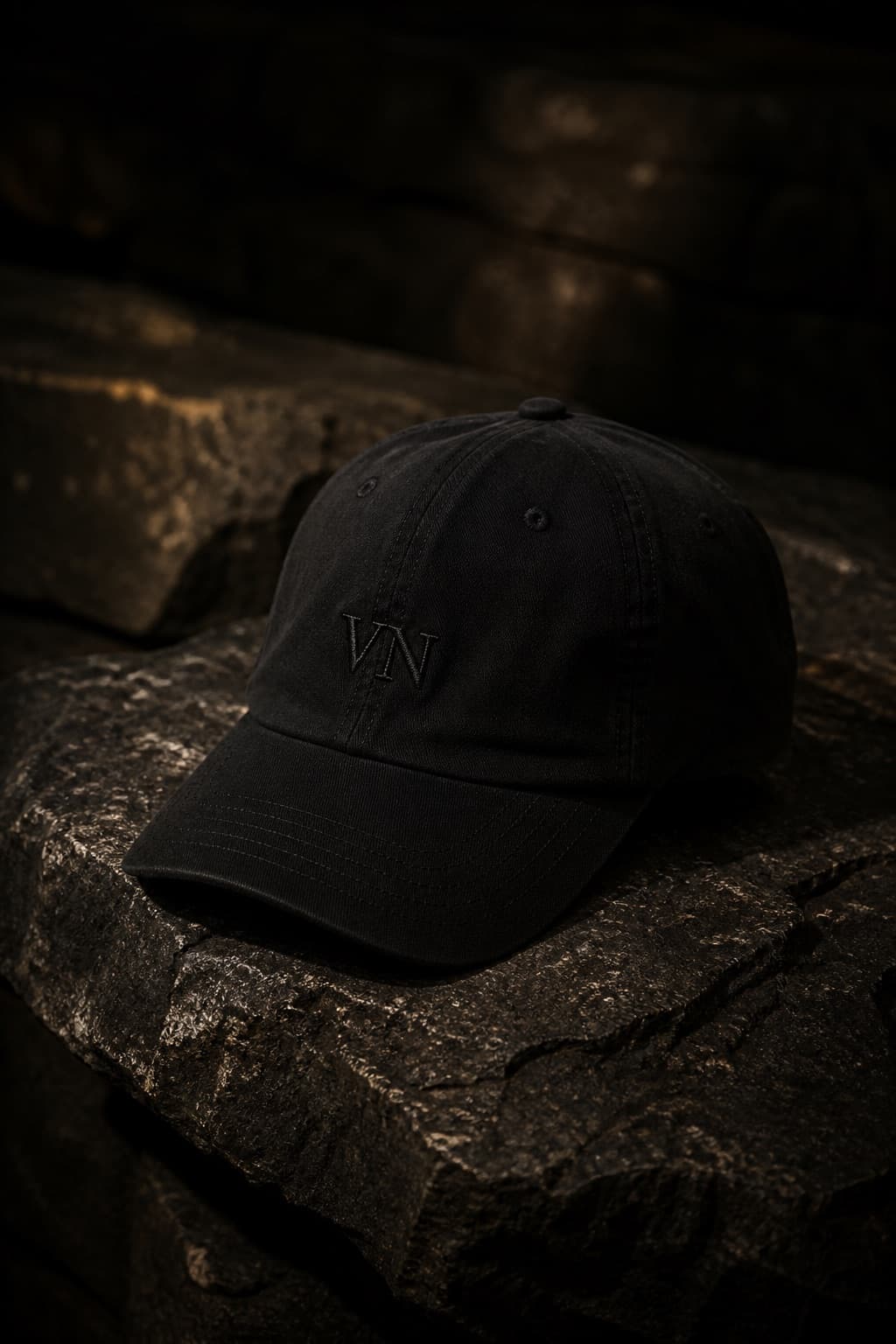 Black low-profile cotton cap on dark limestone, visor catching a warm light