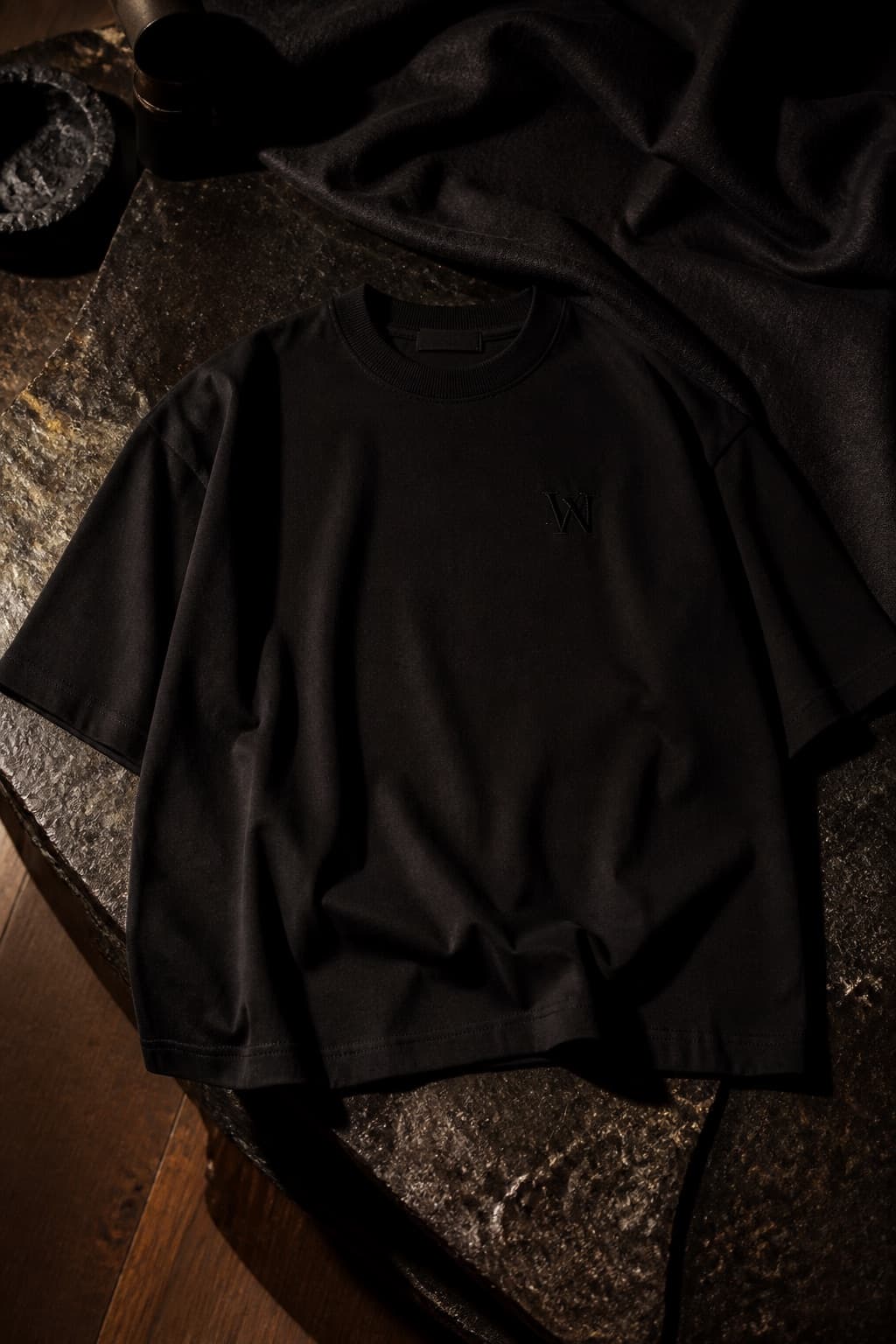 Oversized black boxy t-shirt with drop shoulders, crumpled on black linen at night